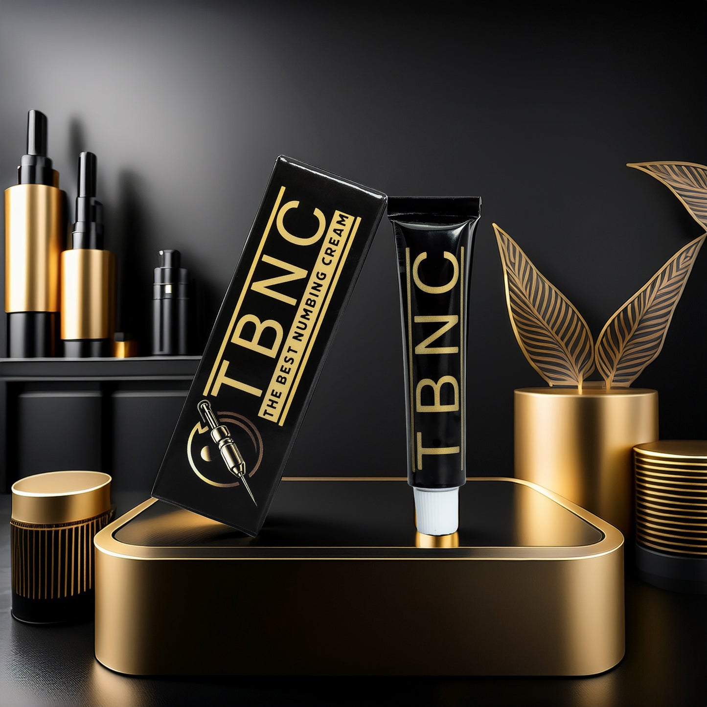 A black and gold tube labeled "TBNC - The Best Numbing Cream Tattoo Numbing Cream" stands upright by its matching box, showcasing lidocaine pain relief for tattoos amid elegant gold accents and abstract leaf decor.