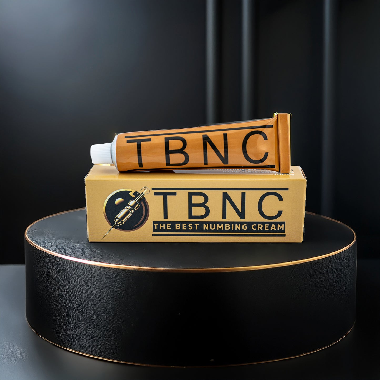 A gold tube labeled "TBNC" sits atop a matching gold box with "TBNC - The Best Numbing Cream" and "Tattoo Numbing Cream XL," emphasizing maximum-strength lidocaine, displayed on a black pedestal against a black background.
