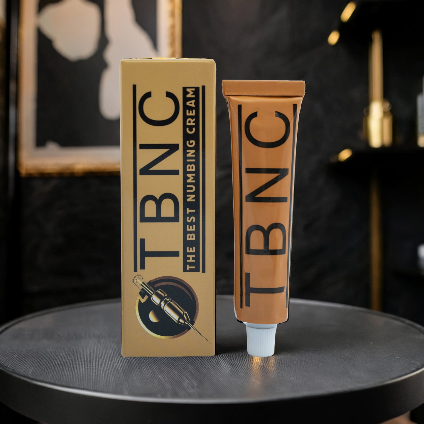 A tube and box of TBNC - The Best Numbing Cream’s Tattoo Numbing Cream XL stand upright on a black surface, with bold black text and a syringe graphic on the packaging against a sleek, dark background. Tattoo artist approved.