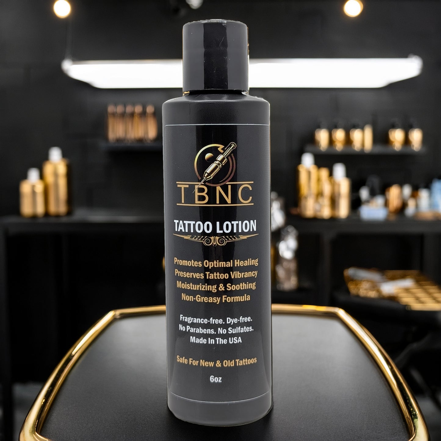 A black bottle of TBNC - The Best Numbing Cream Tattoo Aftercare Lotion - Unscented sits on a counter in a modern studio. The label highlights skin regeneration and moisturizing, making it an ideal aftercare lotion. Shelves blur in the background.