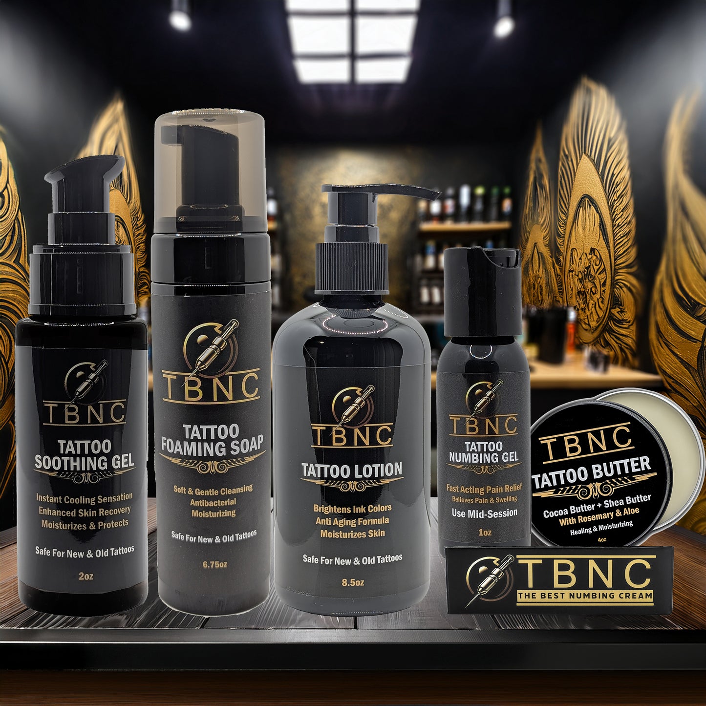 The TBNC - The Best Numbing Cream Tattoo Numbing & Aftercare Bundle, featuring five products, is arranged on a wooden surface with ornate golden wings in the background.