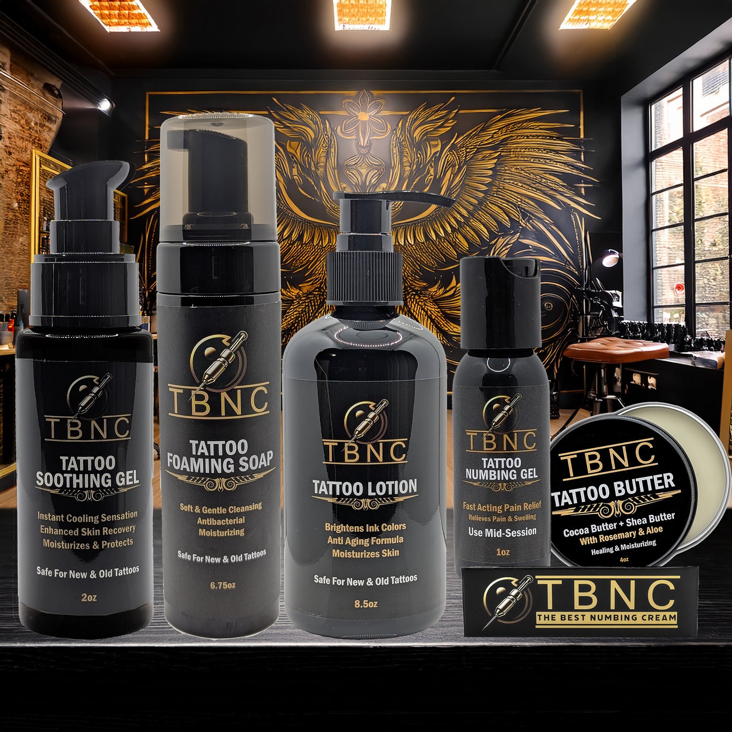 Five black and gold TBNC - The Best Numbing Cream Tattoo Numbing & Aftercare Bundle products—including soothing gel, foaming soap, lotion, numbing gel, and tattoo butter—are displayed before ornate golden wall art in a tattoo studio.
