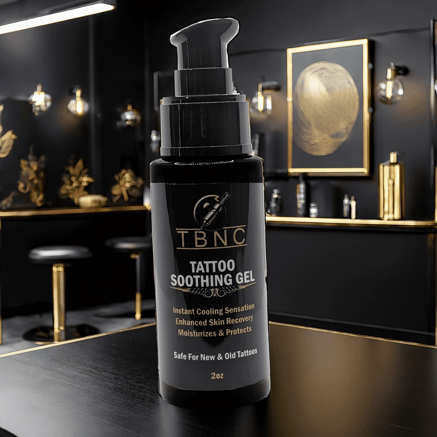 A bottle of TBNC Tattoo Soothing Gel is on a dark countertop in a dimly lit room with gold accents. The label emphasizes its cooling effect, enhanced tattoo vibrancy, and skin recovery benefits. Framed art and pendant lights add to the elegant ambiance.