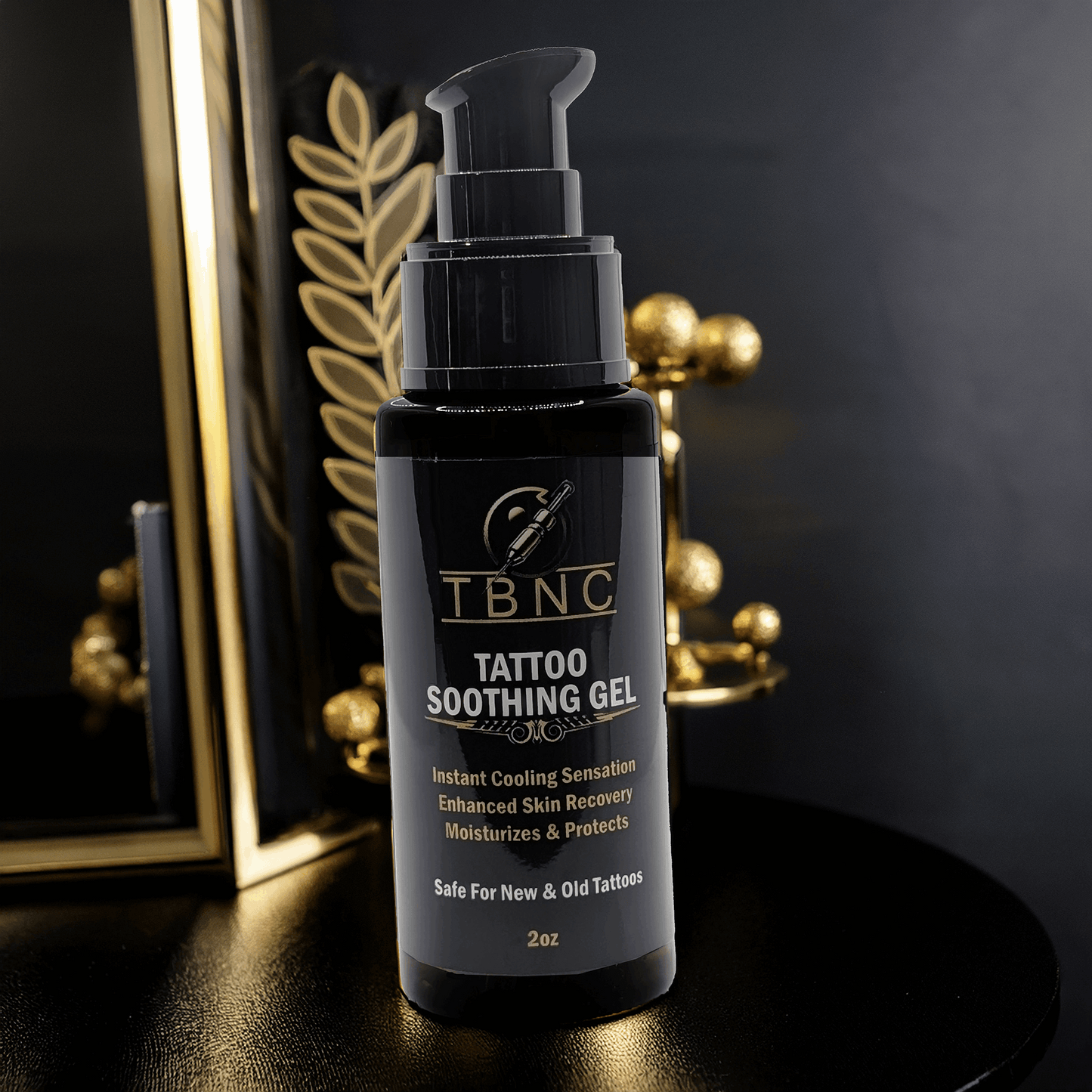 A black bottle of TBNC Tattoo Soothing Gel with a pump dispenser rests on a reflective black surface. Against a dark backdrop with gold elements, it highlights its tattoo healing benefits, enhancing vibrancy and creating a luxurious, calming ambiance.