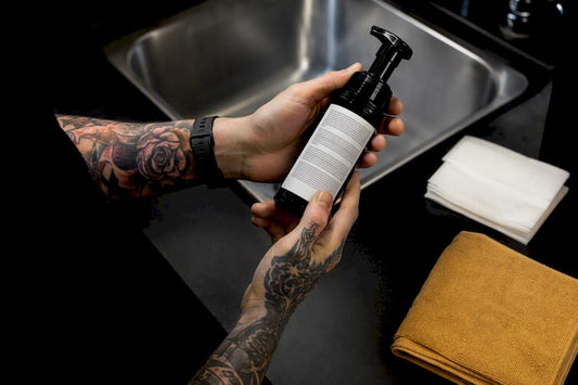 Hands inspecting cleanser beside fresh tattoo