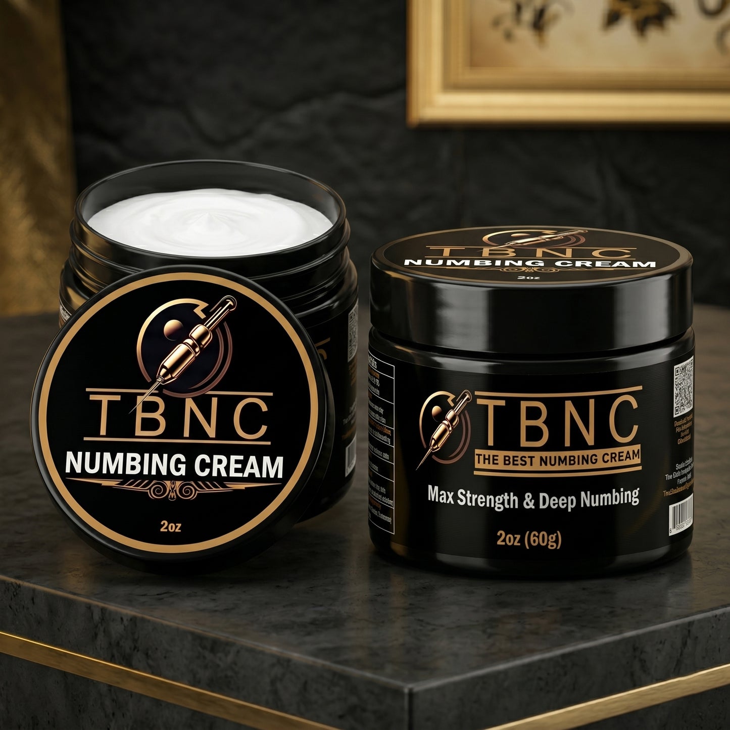 Two sleek black jars of bestselling TBNC Tattoo Numbing Cream MAX, one open to show the white cream, on a dark marble surface.
