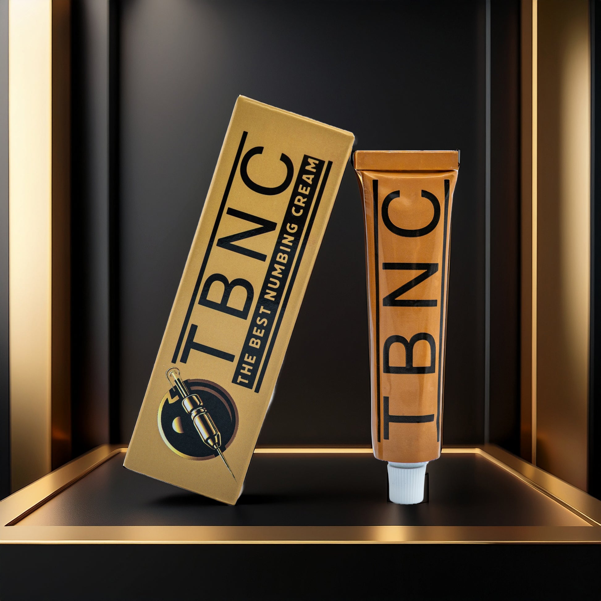 A gold and black box labeled "Tattoo Numbing Cream XL" by TBNC - The Best Numbing Cream sits beside a matching gold tube with "TBNC" printed vertically, both on a sleek shelf—trusted by tattoo artists for maximum comfort.