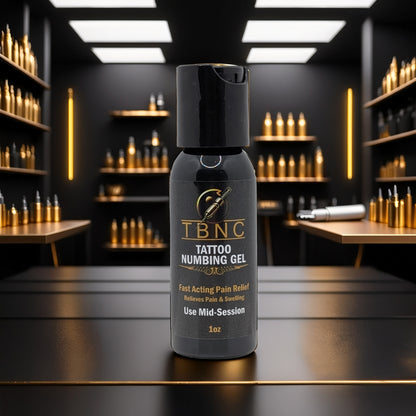 A bottle of TBNC - The Best Numbing Cream Tattoo Numbing Gel - Mid Session, known for fast pain relief, sits in focus on a dark reflective surface. Gold bottles and a tattoo machine appear in the well-lit, modern studio background.