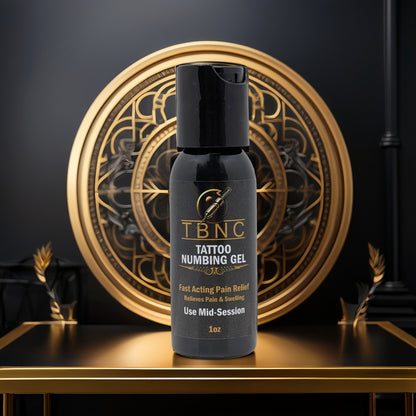 A black bottle of TBNC - The Best Numbing Cream's Tattoo Numbing Gel - Mid Session sits on a black and gold pedestal, with an ornate circular gold design behind. The label highlights Fast Pain Relief and mid-session tattoo numbing.