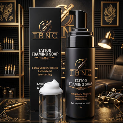 A premium black TBNC Foaming Soap with pump and foam beside it, showcased in a stylish gold room with tattoo gear and chair.