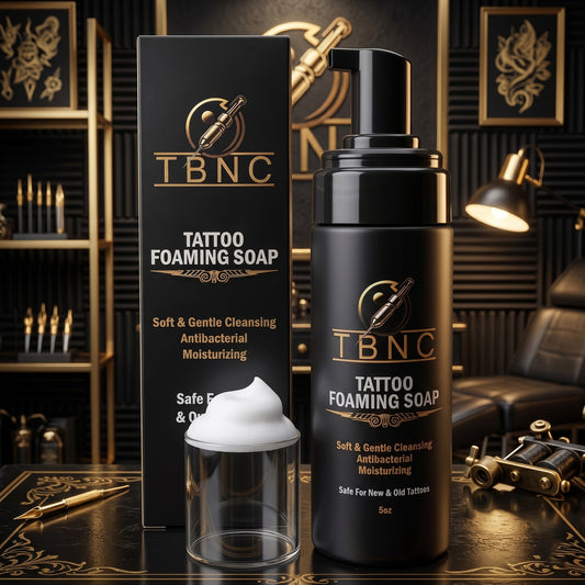 A premium black TBNC Foaming Soap with pump and foam beside it, showcased in a stylish gold room with tattoo gear and chair.