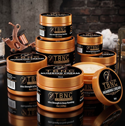 Round containers of the top-selling Tattoo Numbing Cream ULTRA, labeled "Ultra Strength & Deep Numbing," stacked on a dim table; one large jar open to show potent cream inside.