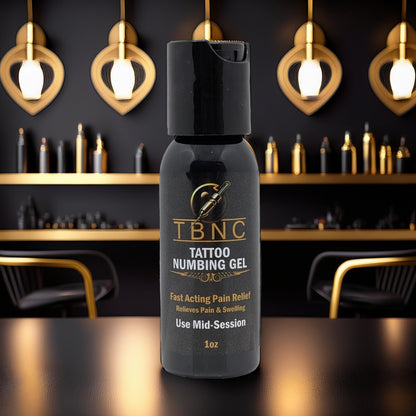 A bottle of TBNC - The Best Numbing Cream Tattoo Numbing Gel - Mid Session rests on a reflective surface in a chic tattoo studio with gold and black decor, highlighted by stylish chairs and wall lights in the background.