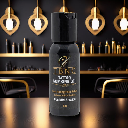 A bottle of TBNC - The Best Numbing Cream Tattoo Numbing Gel - Mid Session rests on a reflective surface in a chic tattoo studio with gold and black decor, highlighted by stylish chairs and wall lights in the background.