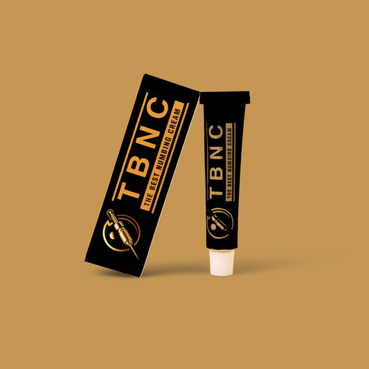 A black and gold box labeled "The Best Numbing Cream - TBNC" stands upright next to a matching tube, both branded with "TBNC - The Best Numbing Cream," set against a tan background. Ideal for painless tattoo sessions.
