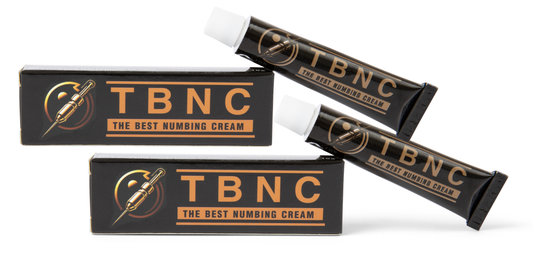 Image of two tubes and two boxes of "The Best Numbing Cream - TBNC - 2 Pack" by TBNC - The Best Numbing Cream. The packaging is black with gold and orange accents. The text on the packaging reads "TBNC - The Best Numbing Cream." There is also an icon of a syringe on the packaging, promising painless tattoos for a comfortable experience.