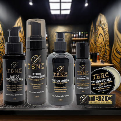 The TBNC - The Best Numbing Cream Tattoo Numbing & Aftercare Bundle, featuring five products, is arranged on a wooden surface with ornate golden wings in the background.