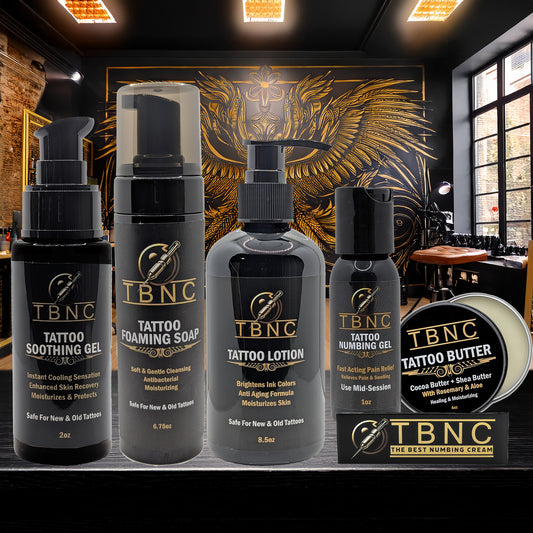 Five black and gold TBNC - The Best Numbing Cream Tattoo Numbing & Aftercare Bundle products—including soothing gel, foaming soap, lotion, numbing gel, and tattoo butter—are displayed before ornate golden wall art in a tattoo studio.