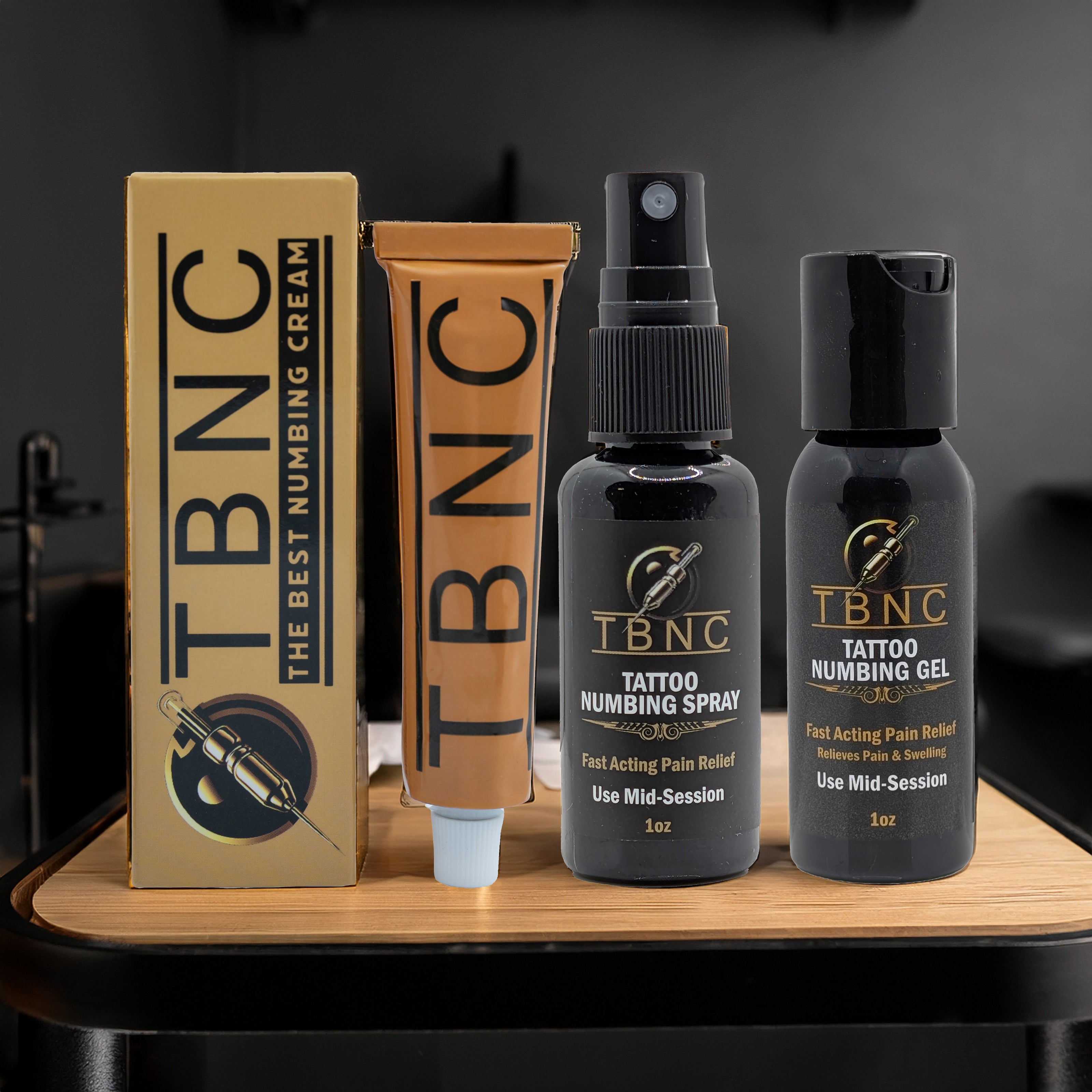 The TBNC - The Best Numbing Cream XL Tattoo Numbing Bundle, featuring four numbing products, is displayed upright on a small wooden table against a dark background.