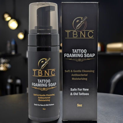 A 5oz bottle and box of TBNC - The Best Numbing Cream Tattoo Foaming Soap, a gentle, antibacterial, and moisturizing cleanser safe for caring for new or old tattoos. Displayed on a dark background.